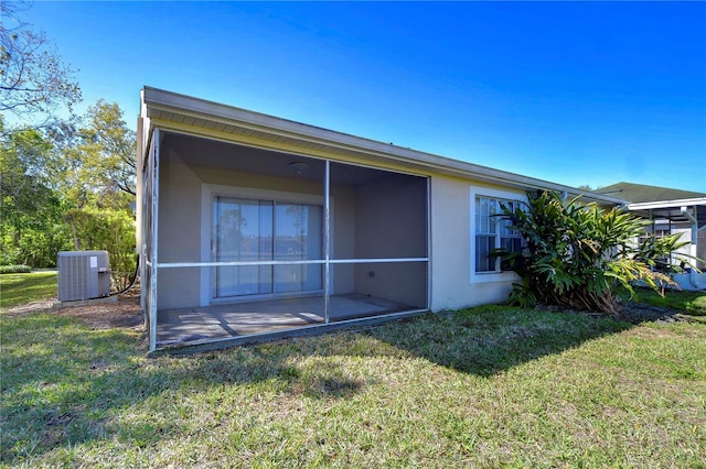 rear view of property featuring central air condition unit, a sunroom, a yard, and stucco siding