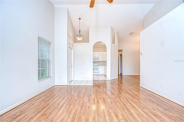34907 Double Eagle Ct, Zephyrhills, FL 33541 - unfurnished living room featuring light wood-style floors, ceiling fan, arched walkways, a towering ceiling, and baseboards