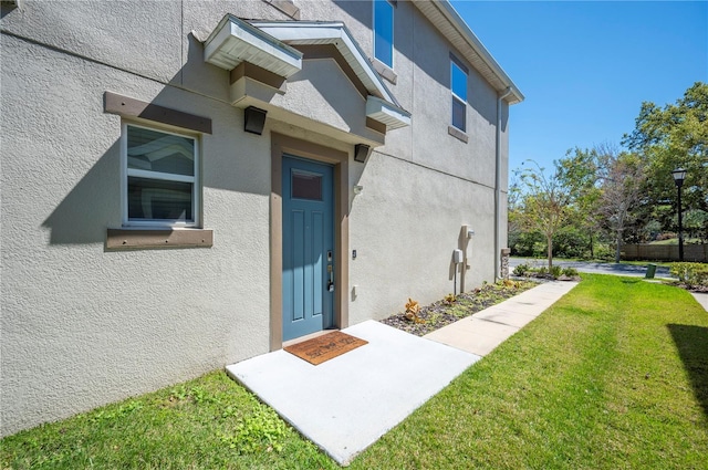 view of exterior entry with stucco siding and a yard