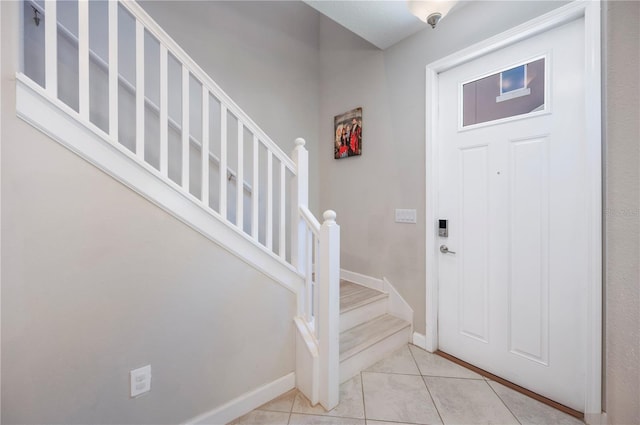 foyer featuring light tile patterned flooring, stairs, and baseboards