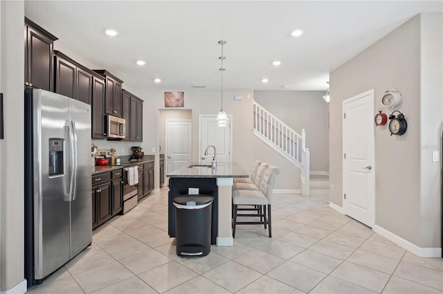 kitchen featuring a sink, a breakfast bar area, dark stone counters, appliances with stainless steel finishes, and a kitchen island with sink