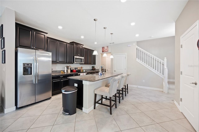 kitchen featuring a center island with sink, a sink, a kitchen breakfast bar, appliances with stainless steel finishes, and light tile patterned flooring