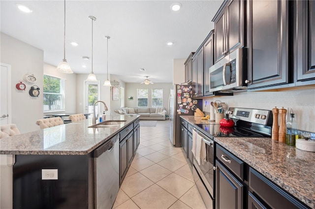 kitchen featuring light stone countertops, a center island with sink, a sink, stainless steel appliances, and open floor plan