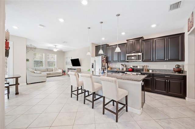 kitchen featuring light tile patterned flooring, an island with sink, stainless steel appliances, a kitchen bar, and open floor plan