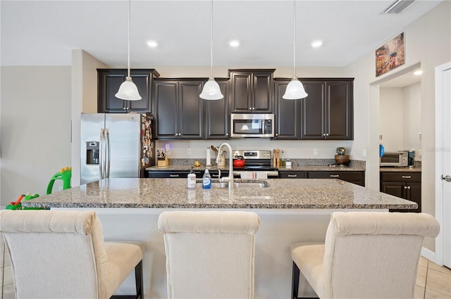 kitchen with a kitchen bar, visible vents, a center island with sink, stainless steel appliances, and light stone countertops