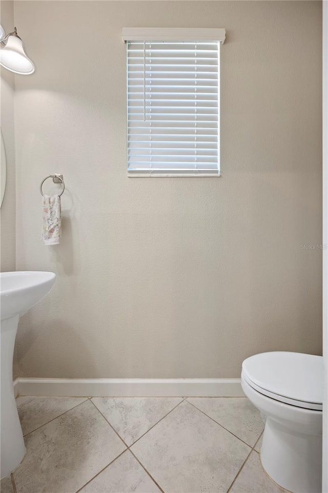 half bath featuring tile patterned flooring, toilet, and baseboards