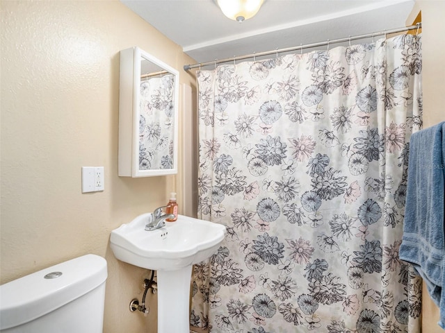 bathroom with toilet, a shower with shower curtain, and a sink