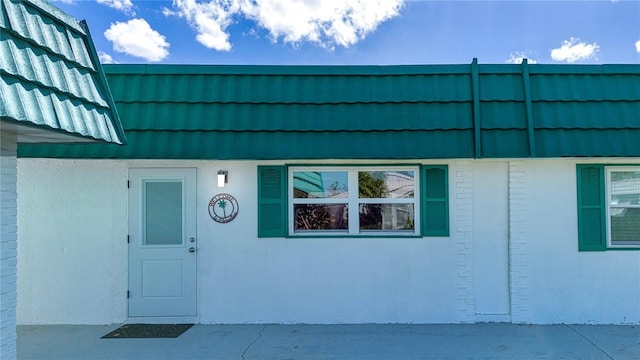 view of exterior entry with a tiled roof, stucco siding, and mansard roof