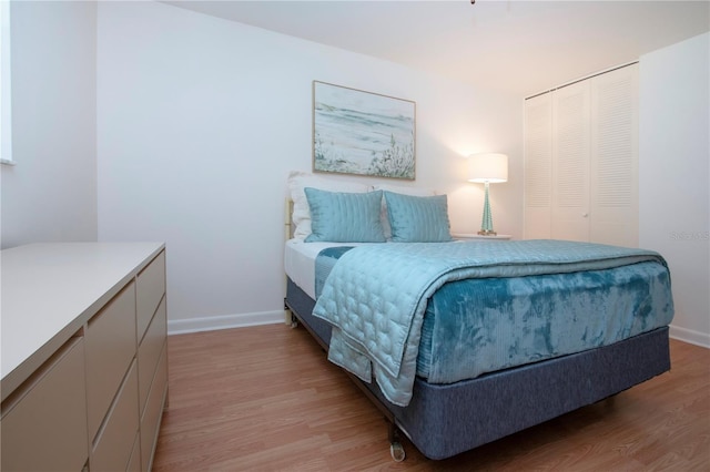 bedroom featuring baseboards, light wood-type flooring, and a closet