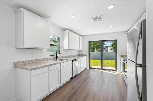 kitchen featuring a sink, dark wood finished floors, stainless steel appliances, white cabinets, and light stone countertops