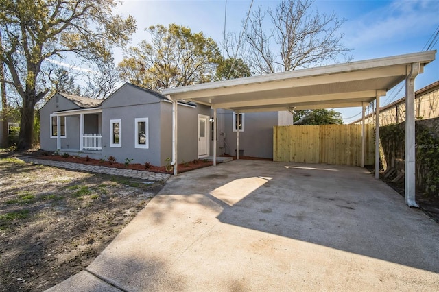 view of front of house featuring a carport, stucco siding, driveway, and fence