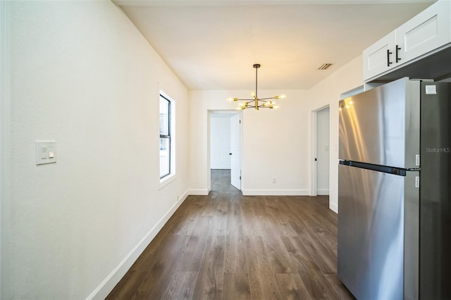 unfurnished dining area featuring an inviting chandelier, dark wood-style floors, visible vents, and baseboards