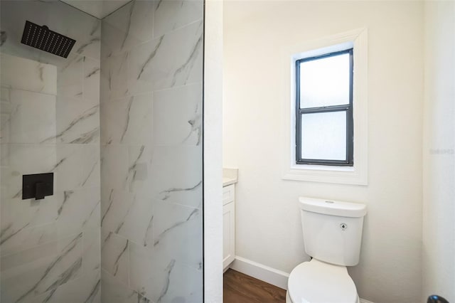 bathroom featuring baseboards, toilet, vanity, wood finished floors, and a marble finish shower