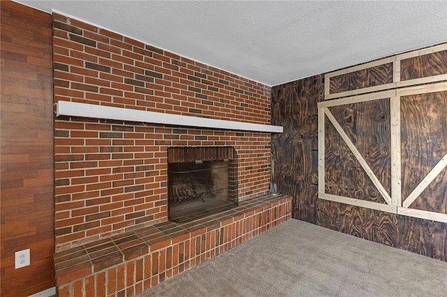 unfurnished living room with carpet flooring, wood walls, a fireplace, and a textured ceiling