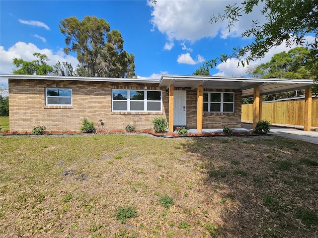 single story home with brick siding, an attached carport, fence, and a front lawn