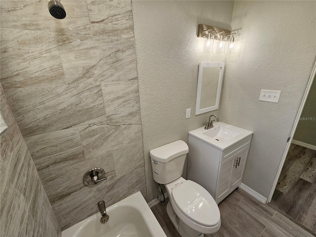 bathroom with toilet, wood tiled floor, a bath, vanity, and a textured wall