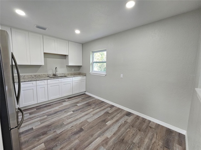 kitchen with baseboards, freestanding refrigerator, light wood-style floors, white cabinetry, and a sink