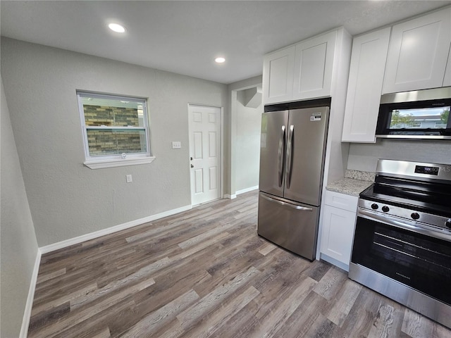 kitchen featuring light wood finished floors, white cabinets, stainless steel appliances, and baseboards