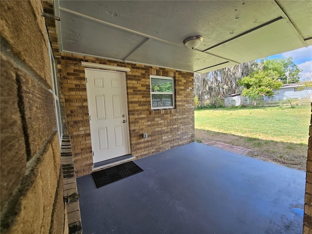 entrance to property with a patio, a lawn, and brick siding