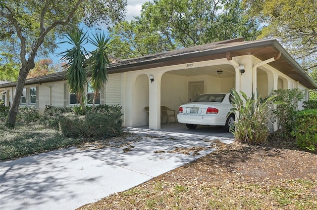 view of side of property featuring brick siding, an attached carport, concrete driveway, and stucco siding
