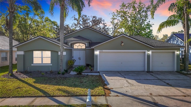 ranch-style home with concrete driveway, stucco siding, a front lawn, a shingled roof, and a garage