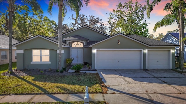 ranch-style home featuring stucco siding, roof with shingles, concrete driveway, a front yard, and a garage