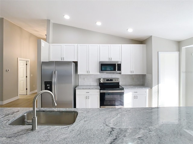 kitchen with light stone countertops, vaulted ceiling, decorative backsplash, appliances with stainless steel finishes, and a sink