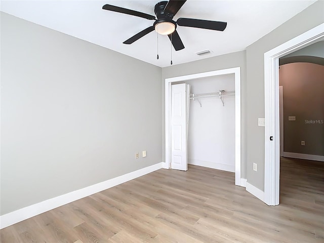 unfurnished bedroom with visible vents, baseboards, a closet, light wood-style flooring, and arched walkways