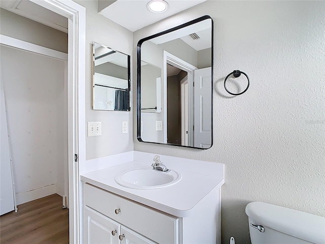 bathroom with visible vents, toilet, wood finished floors, vanity, and a textured wall