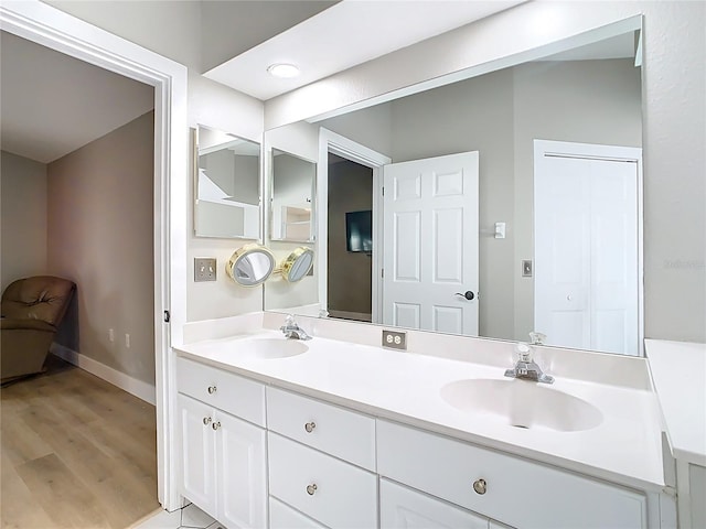 full bath with double vanity, wood finished floors, baseboards, and a sink