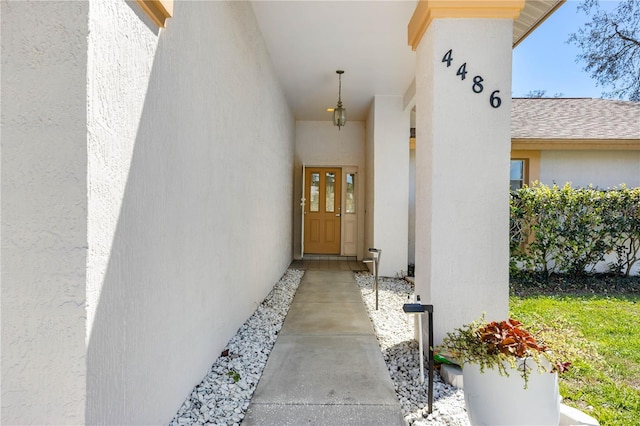 view of exterior entry with stucco siding and a shingled roof