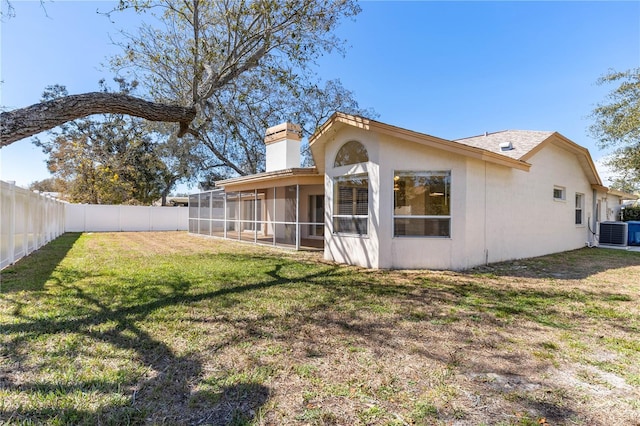 back of property with cooling unit, a fenced backyard, a sunroom, stucco siding, and a lawn