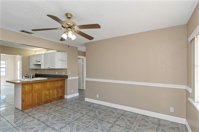 kitchen with visible vents, a peninsula, baseboards, and a ceiling fan