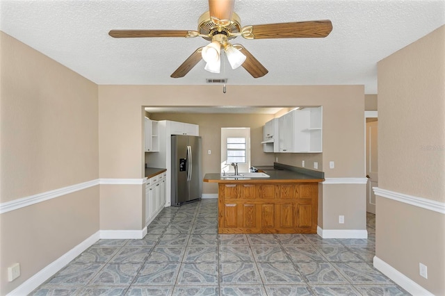 kitchen with visible vents, stainless steel fridge, a peninsula, white cabinets, and ceiling fan