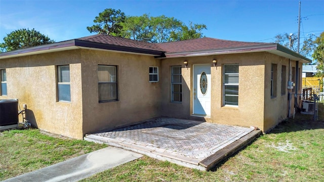 exterior space featuring a patio, cooling unit, roof with shingles, stucco siding, and a front lawn