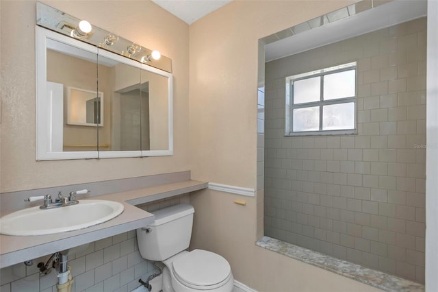 full bathroom with a tile shower, toilet, and a sink