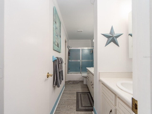 full bath featuring vanity, wood finished floors, baseboards, shower / bath combination with glass door, and crown molding