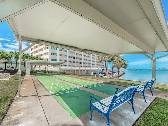 view of property's community with shuffleboard, fence, and a water view