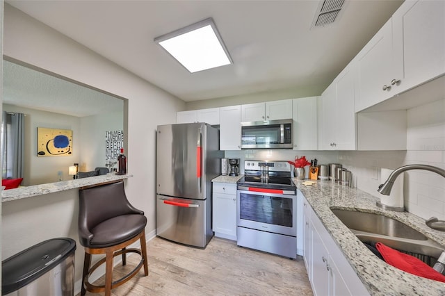 kitchen featuring visible vents, a sink, stainless steel appliances, light wood-style floors, and white cabinetry