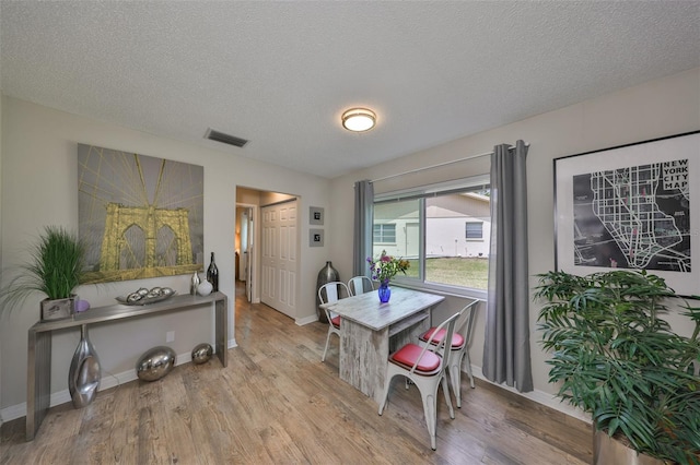 dining room featuring visible vents, a textured ceiling, baseboards, and wood finished floors