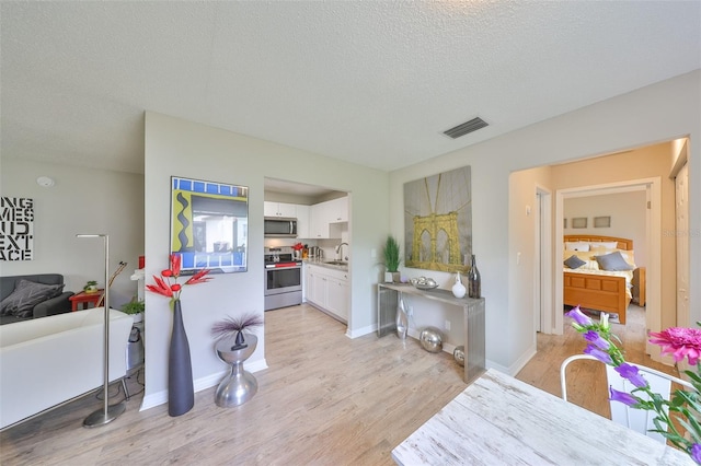 kitchen featuring visible vents, a sink, white cabinetry, stainless steel appliances, and light wood finished floors