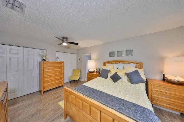 bedroom with visible vents, two closets, wood finished floors, and a textured ceiling