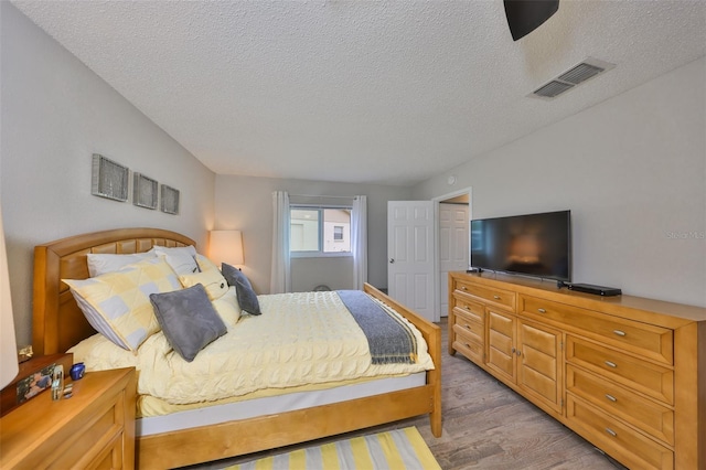 bedroom featuring light wood-style flooring, visible vents, and a textured ceiling