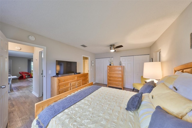 bedroom featuring visible vents, baseboards, multiple closets, wood finished floors, and a ceiling fan