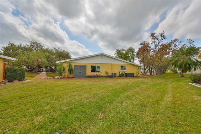 back of property with a lawn, central AC, and stucco siding