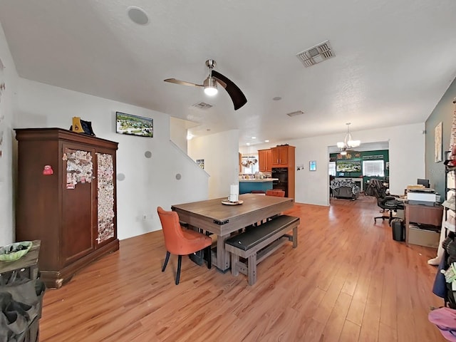 dining area with visible vents, light wood-style floors, and ceiling fan with notable chandelier