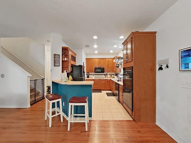 kitchen with light wood-type flooring, a kitchen breakfast bar, black appliances, and a peninsula