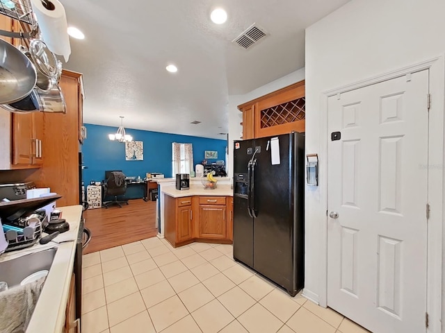 kitchen with light tile patterned floors, visible vents, light countertops, black fridge with ice dispenser, and open floor plan