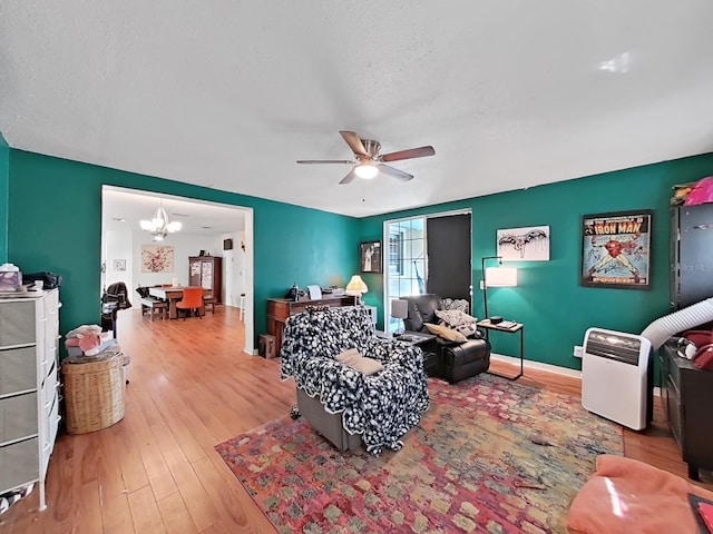 living area with baseboards, wood finished floors, and ceiling fan with notable chandelier