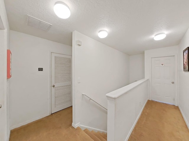 hallway featuring visible vents, an upstairs landing, light carpet, a textured ceiling, and baseboards